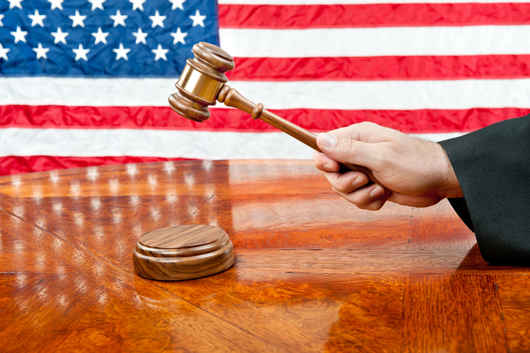 A judge’s gown and gavel with sound block on deep, rich colored wooden desktop and American flag